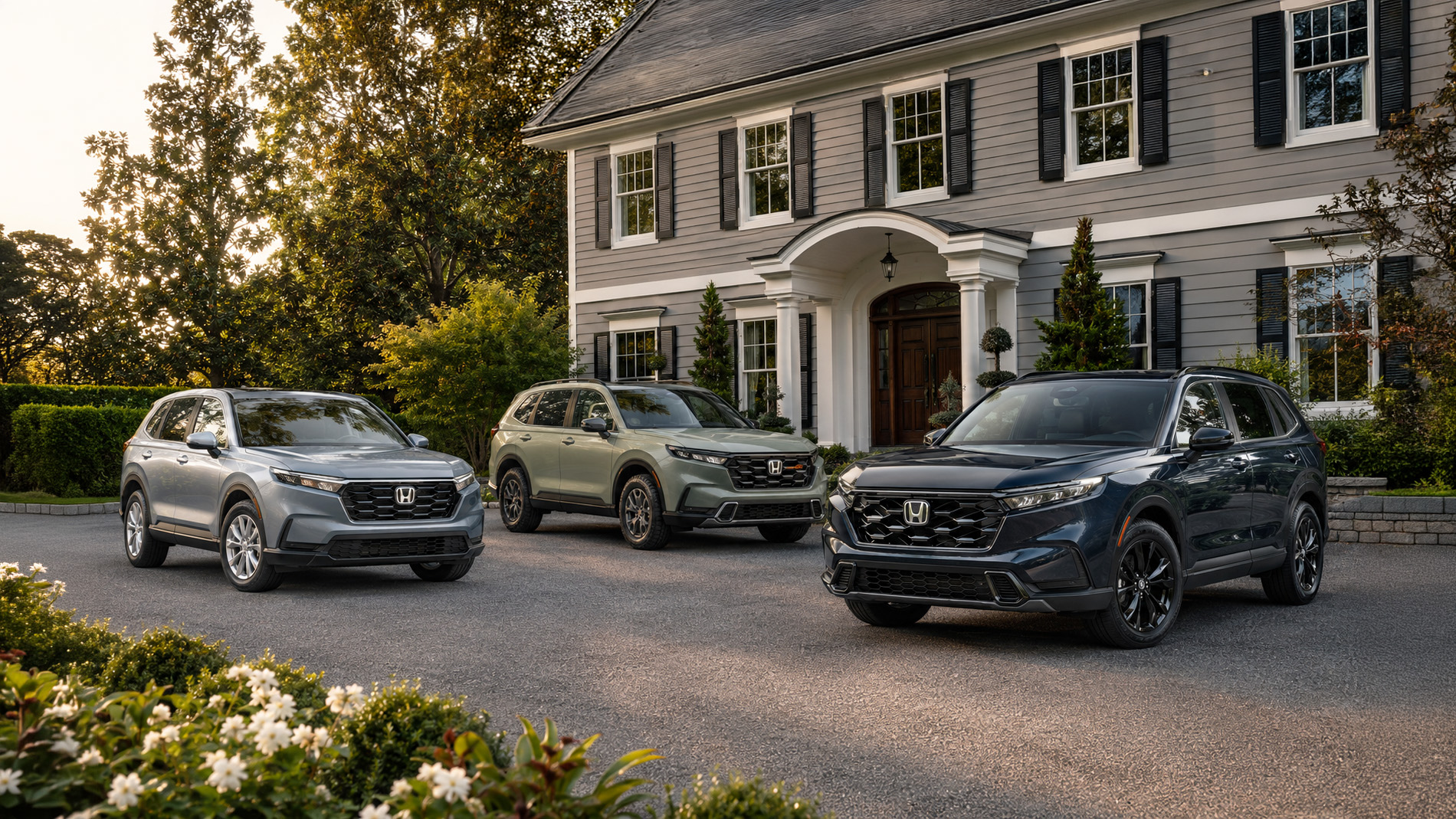 Three 2026 Honda CR-V SUVs in silver, green, and blue parked side by side in a residential driveway at sunrise, with a gray colonial-style home and trees in the background, illustrating the SUV’s refined styling and trim variety.