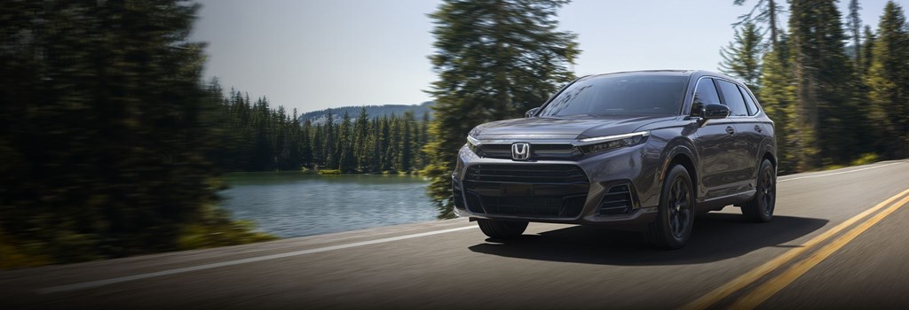 2026 Honda CR-V colors shown in blue driving by a lake in the pine trees