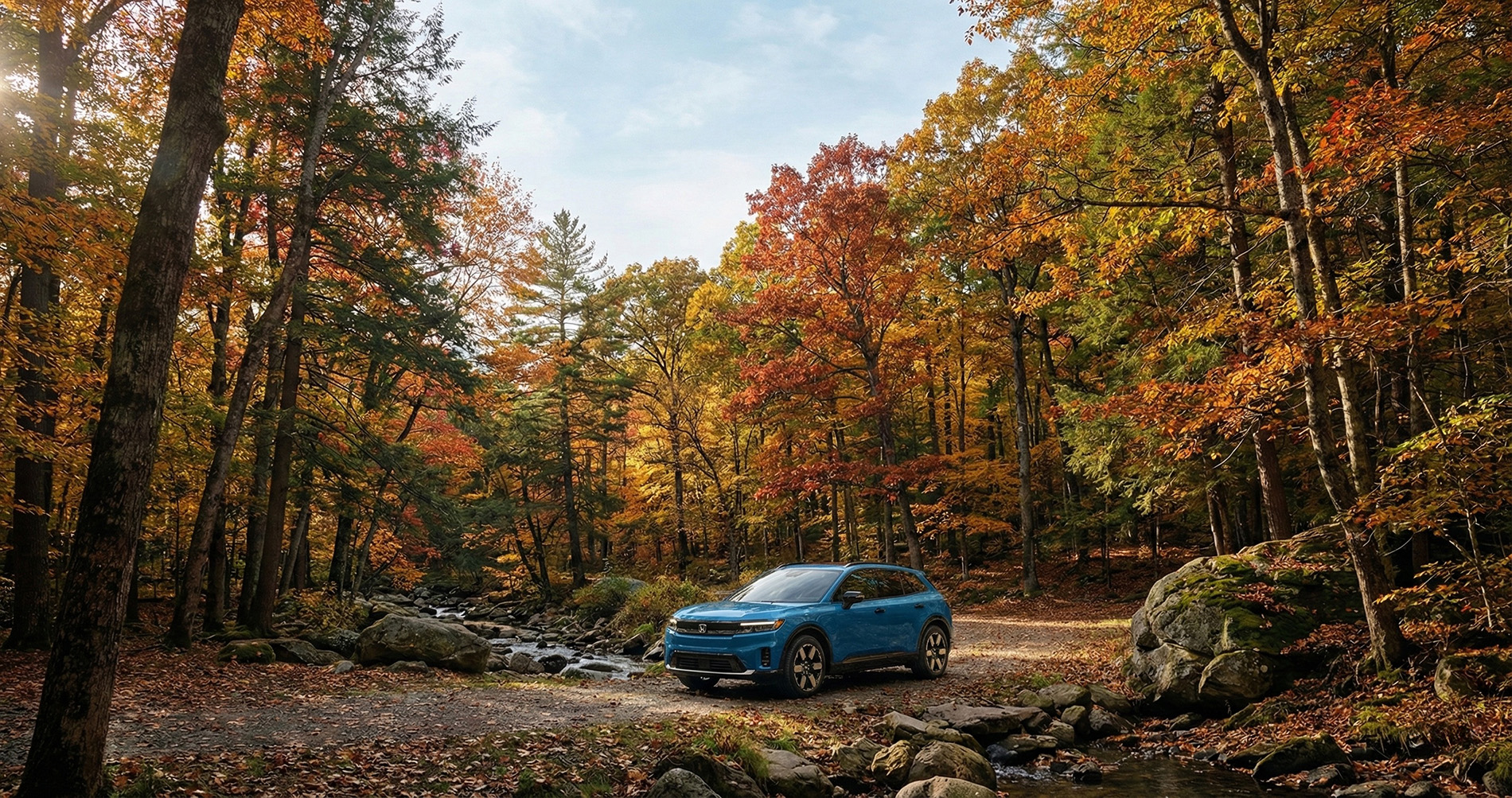 A blue 2026 Honda Prologue trim level parked in a forrest with the tree in autumn colors