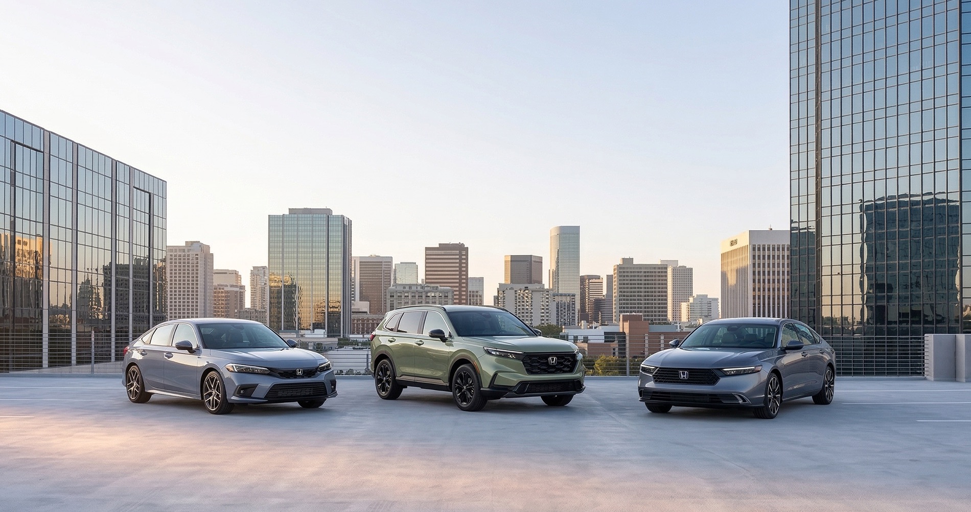 Honda Civic sedan, Honda CR-V SUV, and Honda Accord sedan parked on a rooftop parking garage with a city skyline in the background