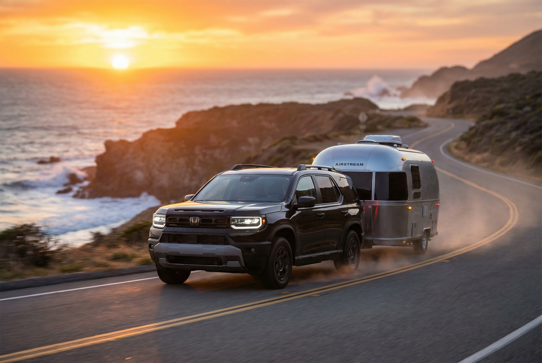 2026 Honda Passport towing an Airstream travel trailer along a winding coastal road at sunset, demonstrating towing capability.