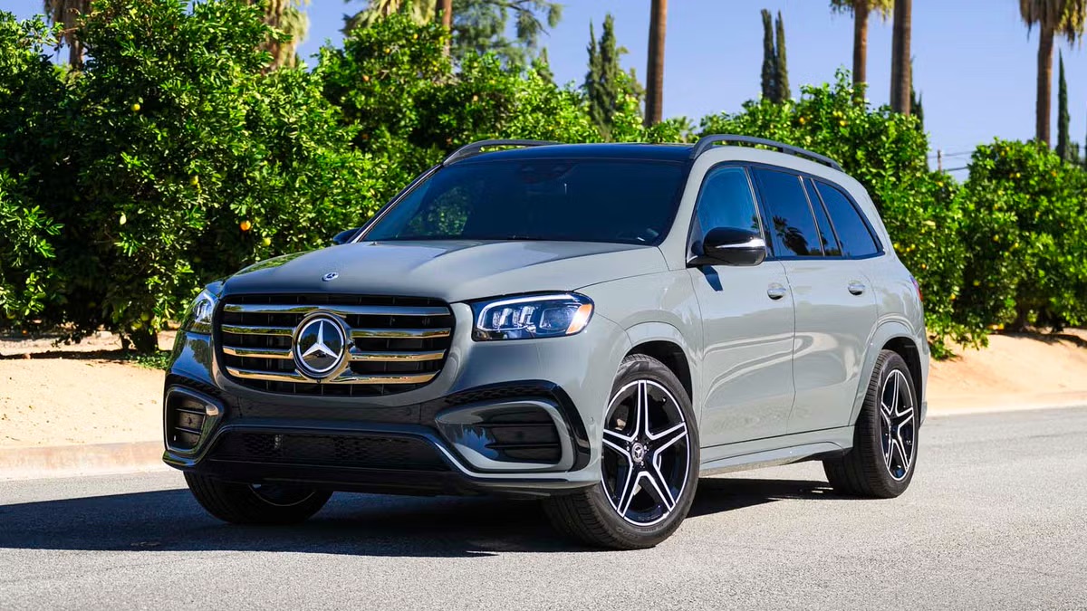 2026 Mercedes-Benz GLS driving on a palm-lined road, shown from a front three-quarter angle with signature grille design, upscale three-row luxury SUV proportions, and refined road presence