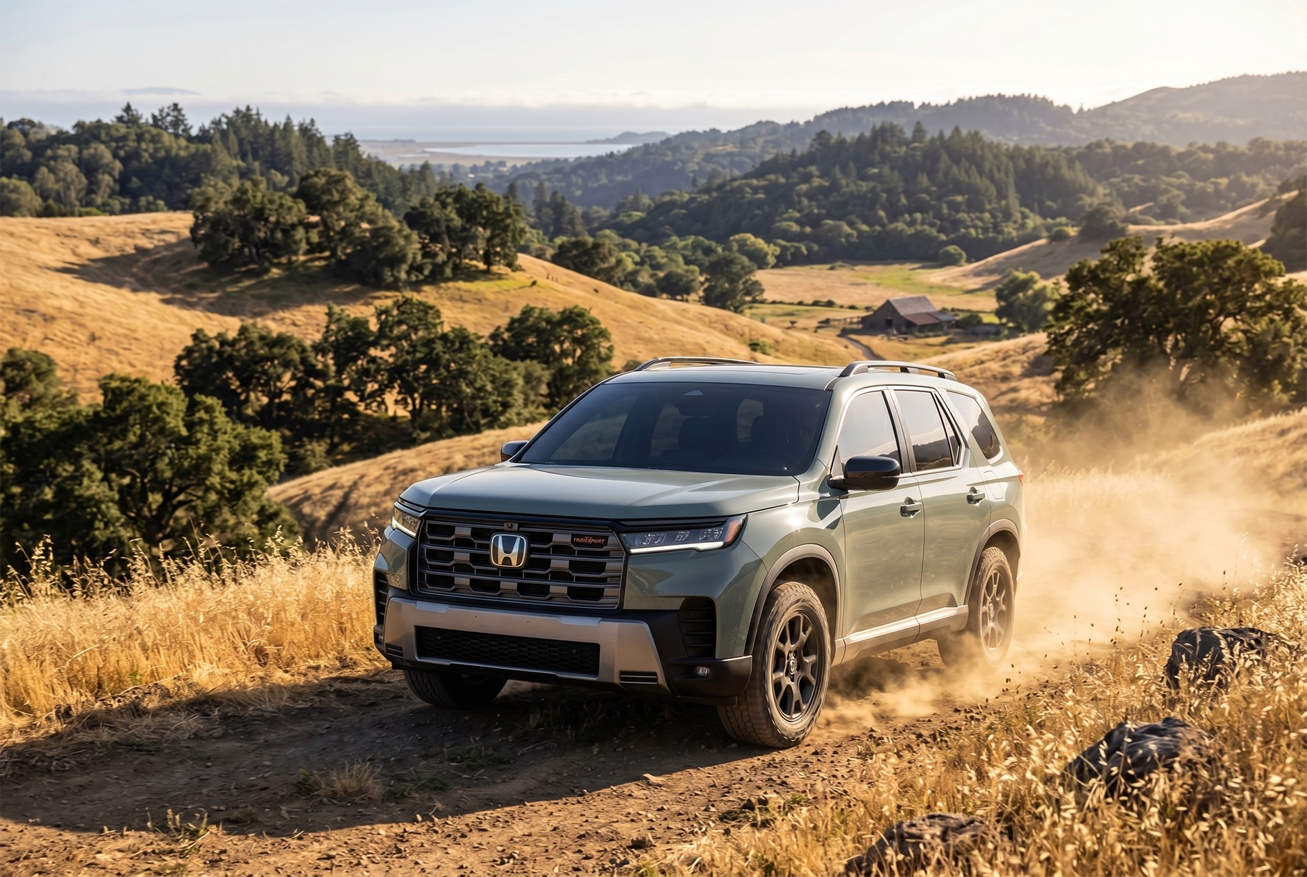 2026 Honda Pilot TrailSport trim level kicking up dust on a dirt trail through rolling hills, with dry grass, scattered trees, and a barn in the distance under a clear sky.