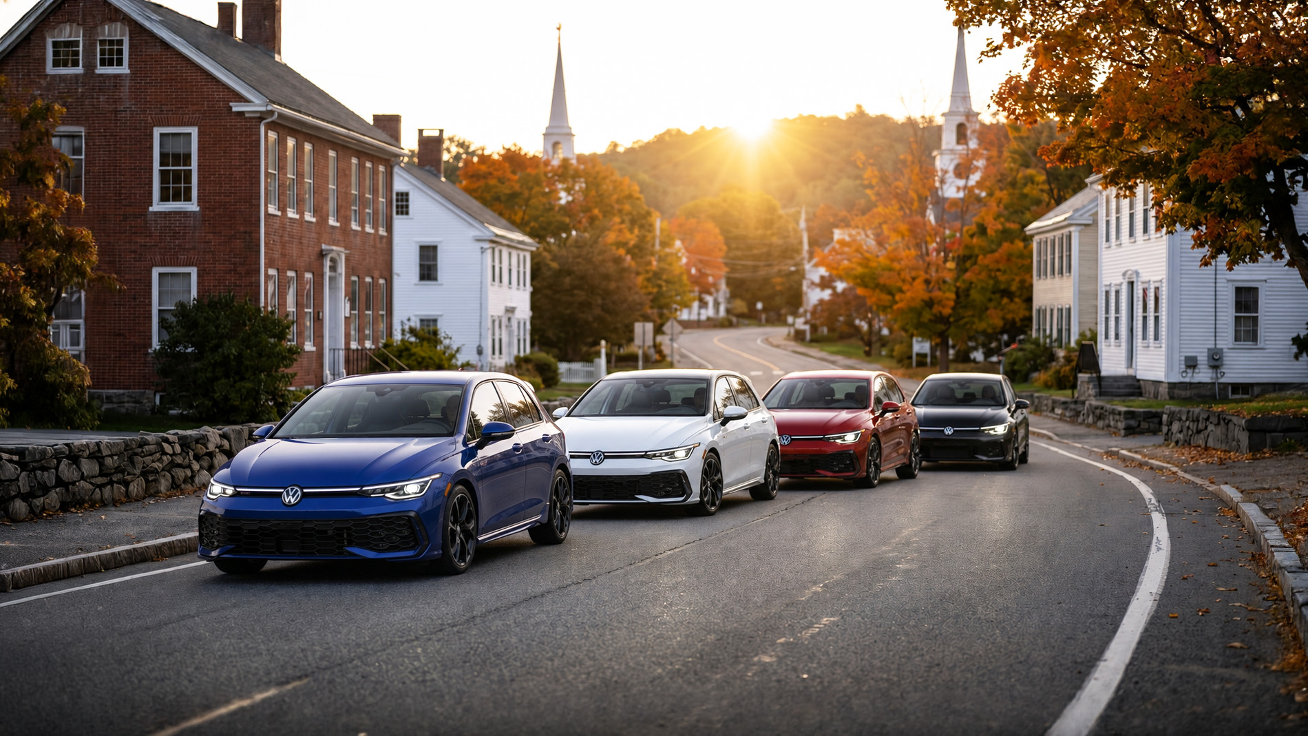 Four 2026 Volkswagen Golf Hatchbacks In Blue, White, Red, And Black Drive Along A Curving Street Lined With Brick And White Colonial‑Style Buildings At Sunrise, With Autumn Trees And Church Steeples In The Background, Showcasing The GTI And R Trim Levels.