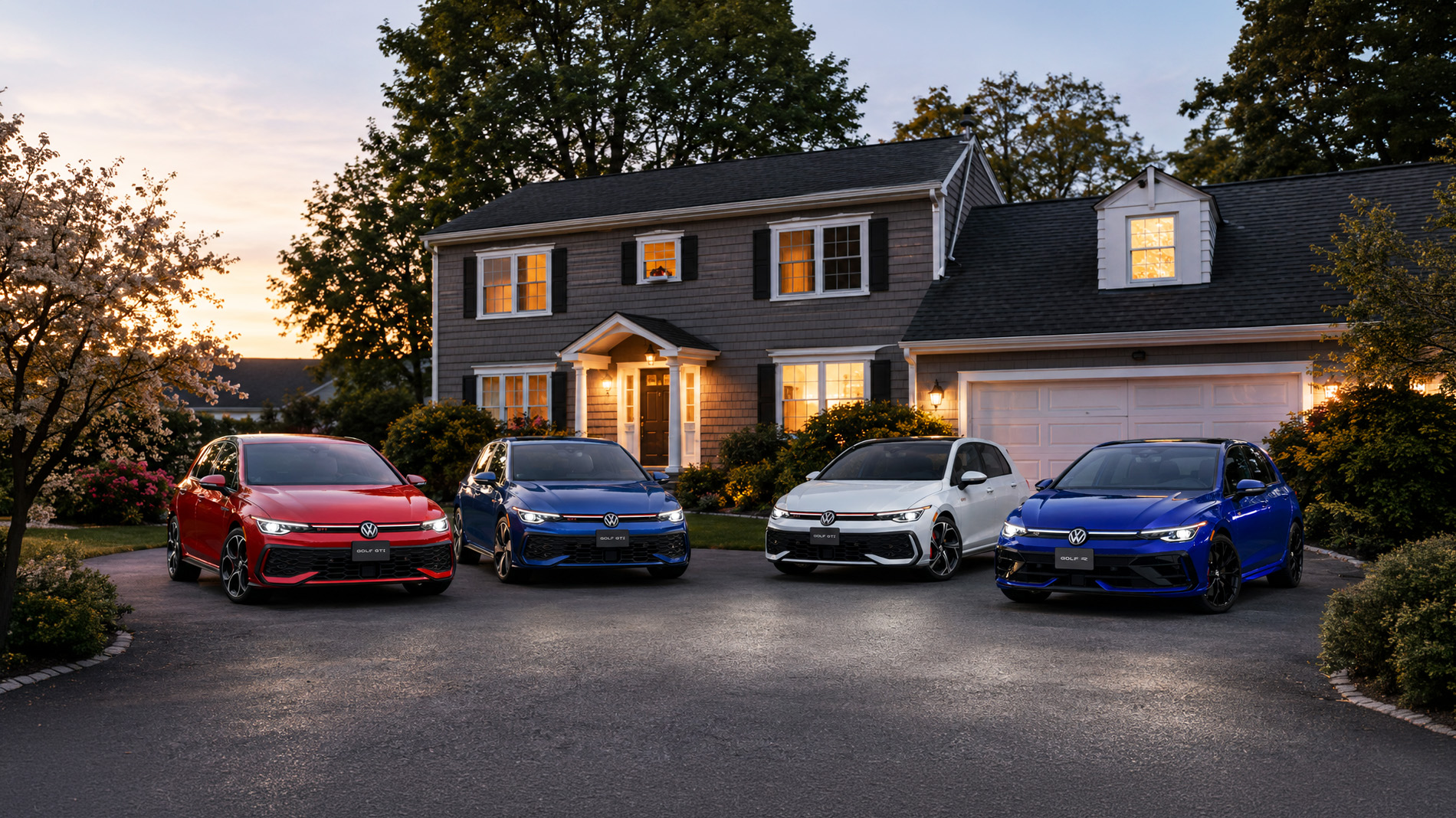 Four 2026 Volkswagen Golf hatchbacks in red, blue, white, and gray parked side by side in a residential driveway at dusk, with warm house lights and trees in the background, highlighting the sporty design and color range of GTI and R models.