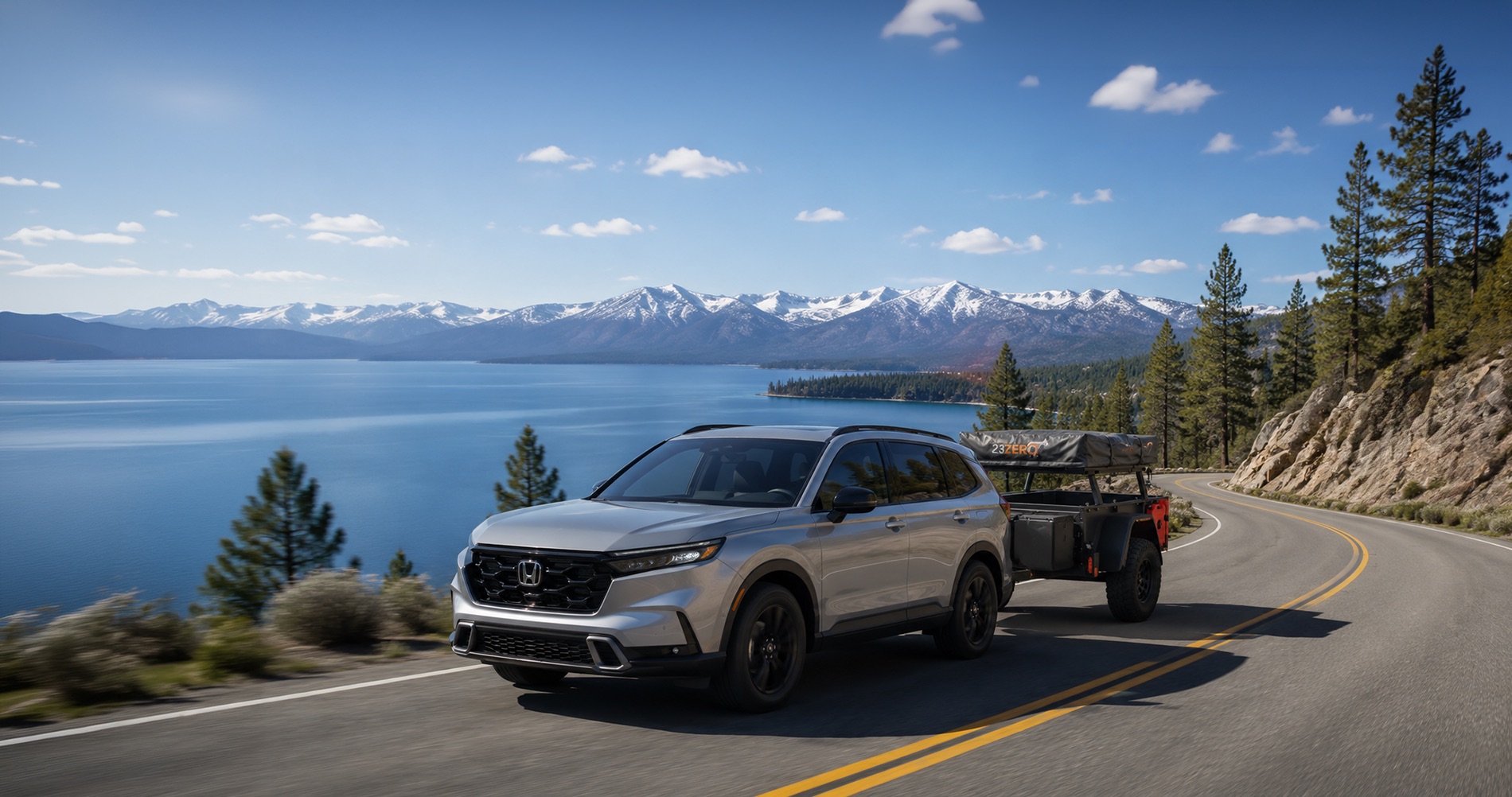 2026 Honda CR-V towing a compact overland camping trailer along a mountain highway near Lake Tahoe, with pine trees, lake views, and Sierra Nevada peaks in the background.