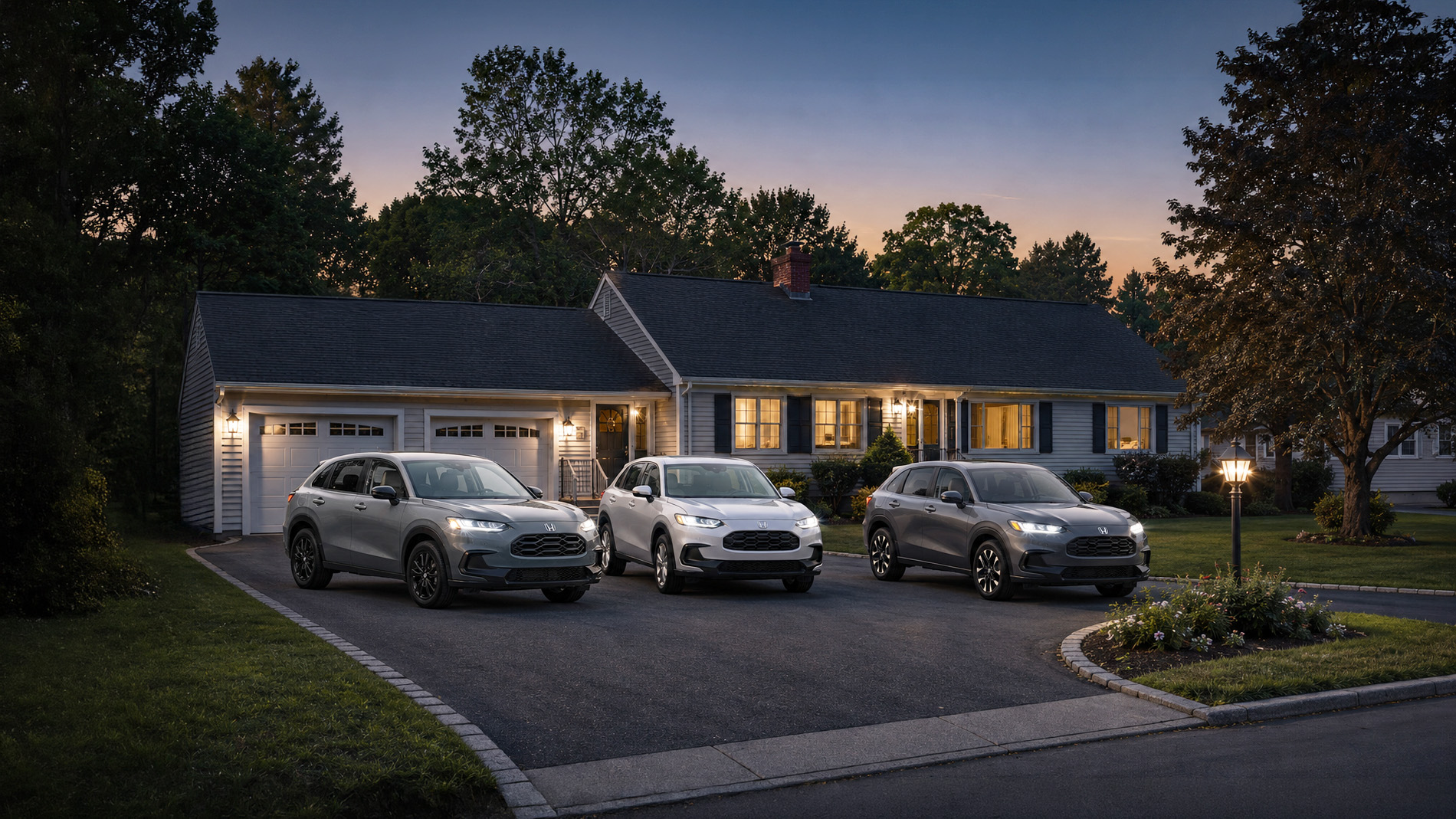 Three 2027 Honda HR‑V SUVs in silver, white, and gray parked side
by side in a residential driveway at dusk, with warm porch lights and
trees in the background, showcasing the range of HR‑V trim levels for
everyday use.