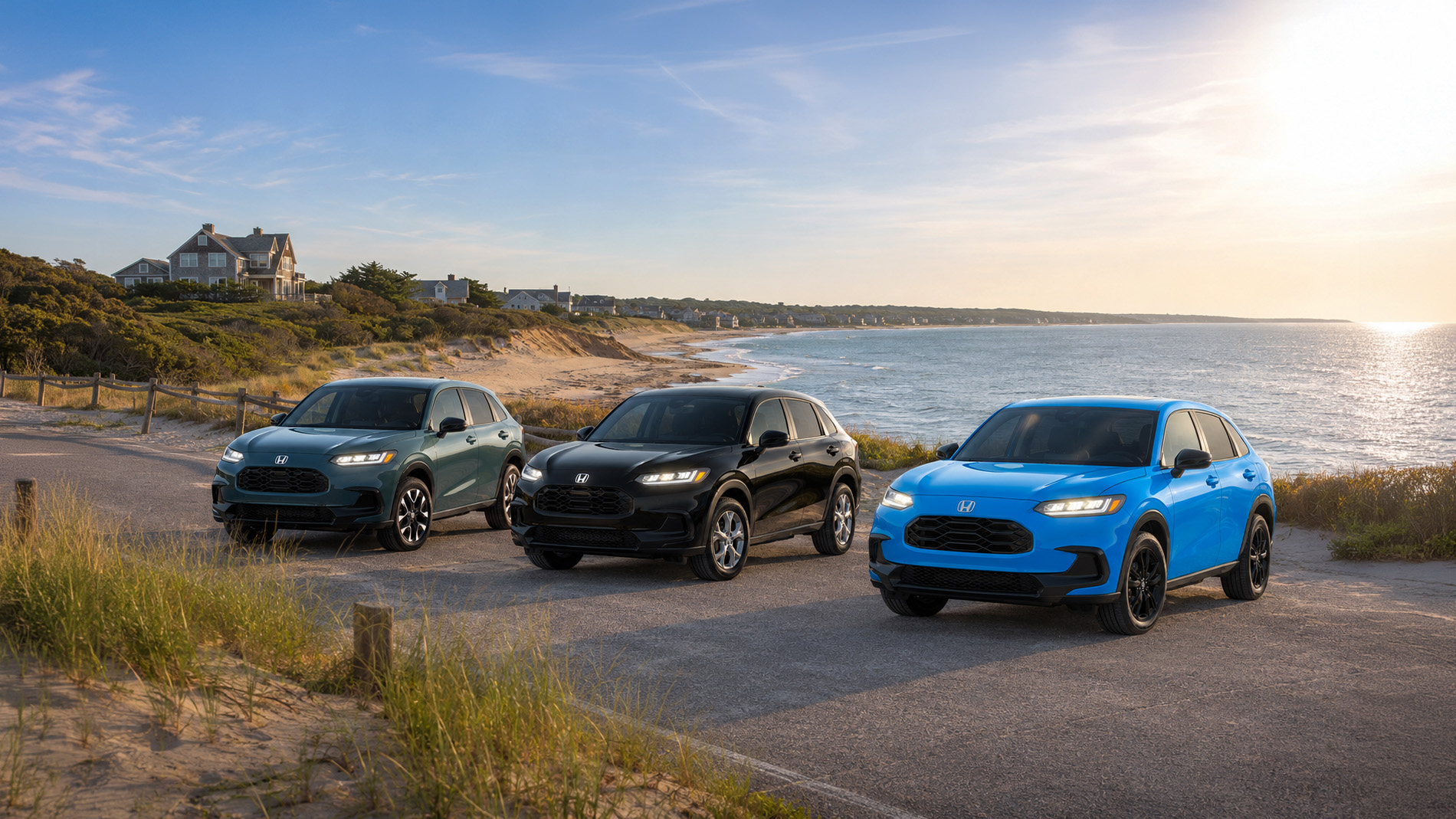 Three 2027 Honda HR‑V SUVs in green, black, and bright blue parked near a beach at sunset, with ocean waves and coastal homes in the background, illustrating style and versatility across HR‑V trim levels.