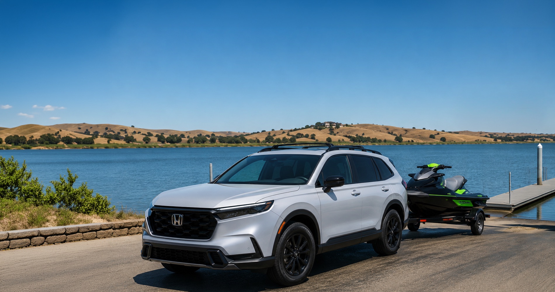 White 2026 Honda CR-V parked beside the Discovery Bay marina towing a black and green jet ski on a trailer, with rolling golden California hills, calm waterfront views, and a Discovery Bay sign in the background under a clear blue sky.