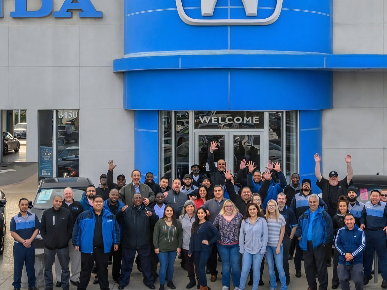 Tracy Honda dealership staff gathered outside the Honda showroom entrance in Tracy, California, with sales, service, and support team members standing together in front of the blue Honda tower and dealership building.