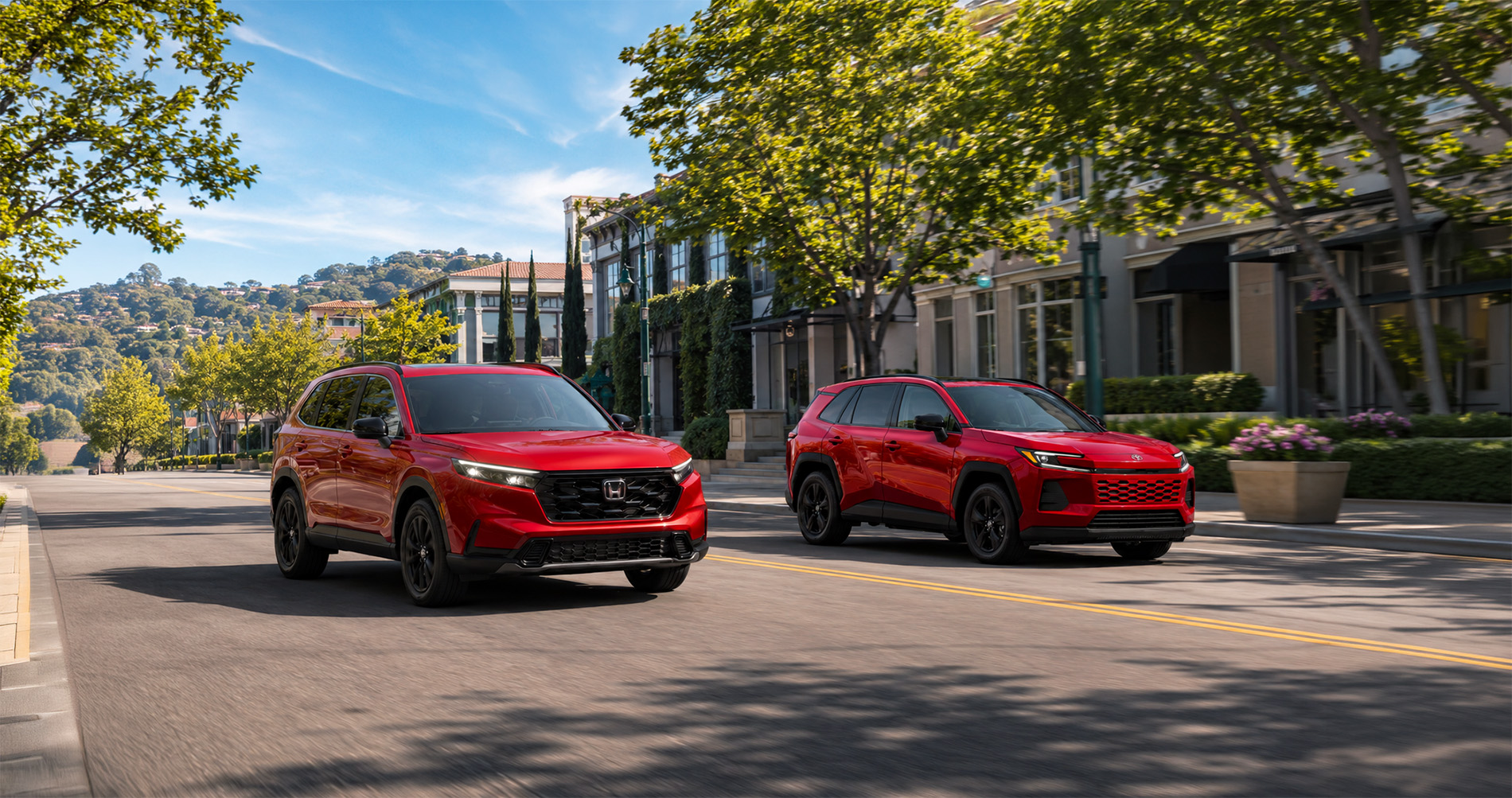 Two red SUVs—a 2026 Honda CR-V and a 2026 Toyota RAV4—driving side by side through downtown El Cerrito, California, with tree-lined streets, modern storefronts, and hills in the distance, emphasizing their sporty design and urban versatility.