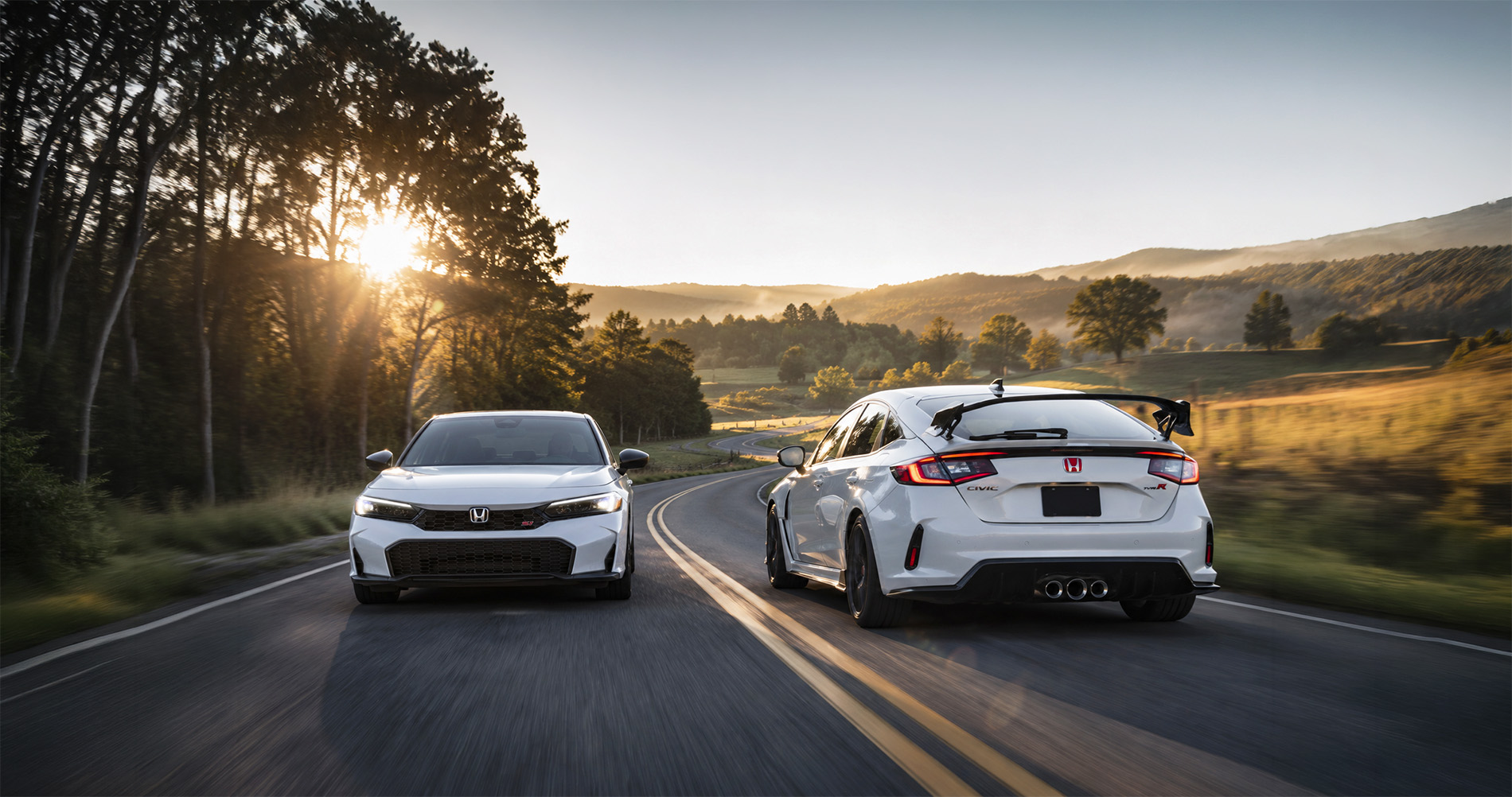 Two white Honda Civics—a Civic Si sedan and a Civic Type R hatchback—driving along a winding country road at sunrise near Troy, New York, with tall trees, open fields, and rolling hills in the background, highlighting the contrast between everyday Civic trims and the performance-focused Civic Type R.