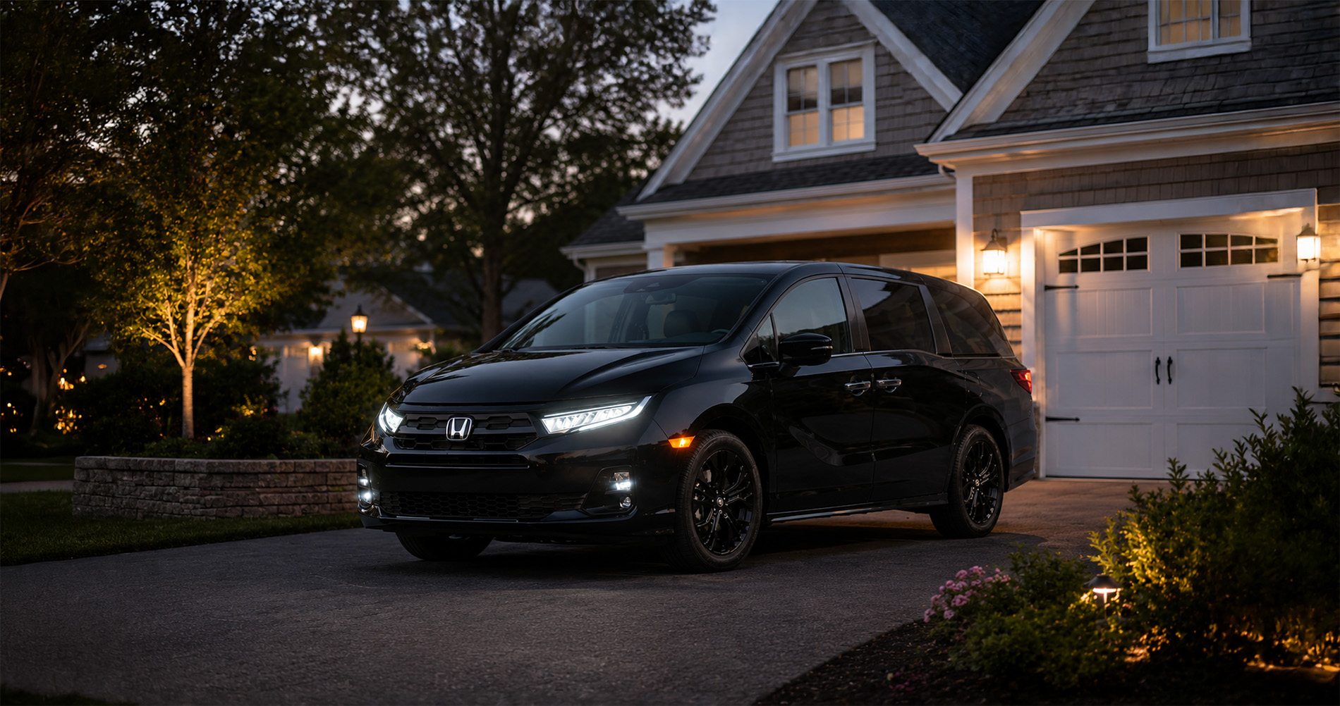 A black Odyssey parked in a well-lit suburban driveway at dusk, highlighting its upscale design.