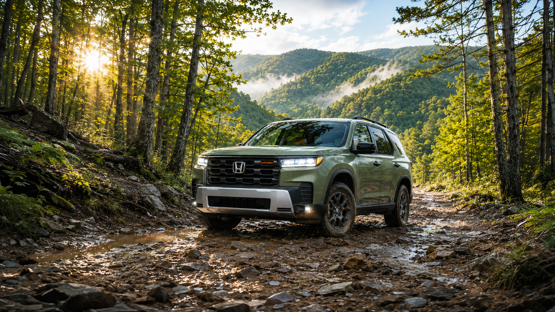 A green 2026 Honda Pilot TrailSport drives along a muddy forest trail surrounded by trees and sunlight filtering through the hills of rural Kentucky, illustrating the SUV’s off-road capability and adventurous design.