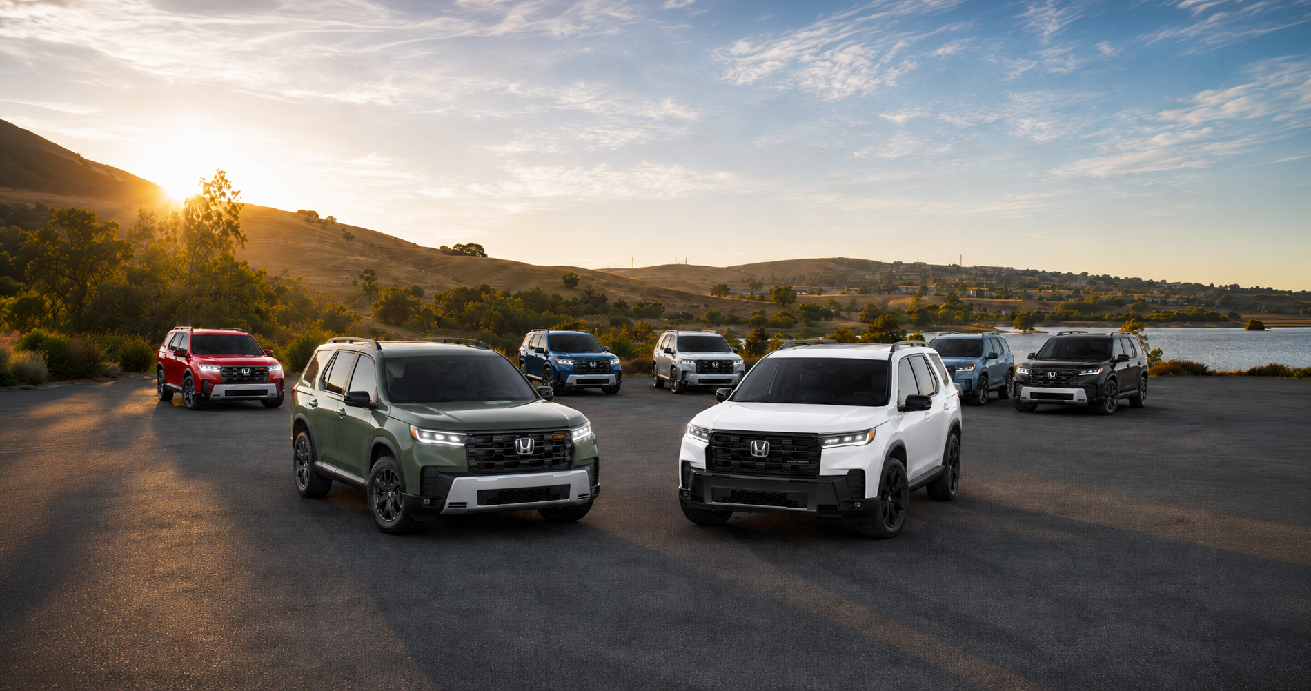 Seven 2026 Honda Pilot SUVs in white, green, red, blue, silver, and black parked side by side near a lakeside overlook in Pittsburg, California, with rolling hills and trees in the background under a golden sunset sky, showcasing the full range of Pilot trim levels and color options.