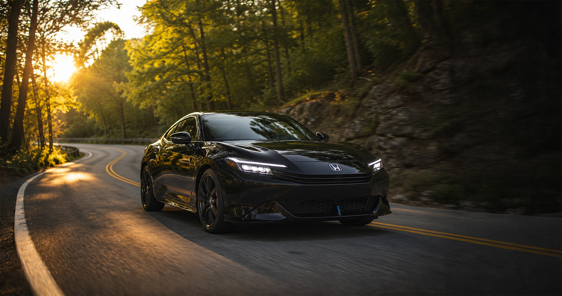 A black 2026 Honda Prelude driving along a winding forest road near Raynham, Massachusetts.