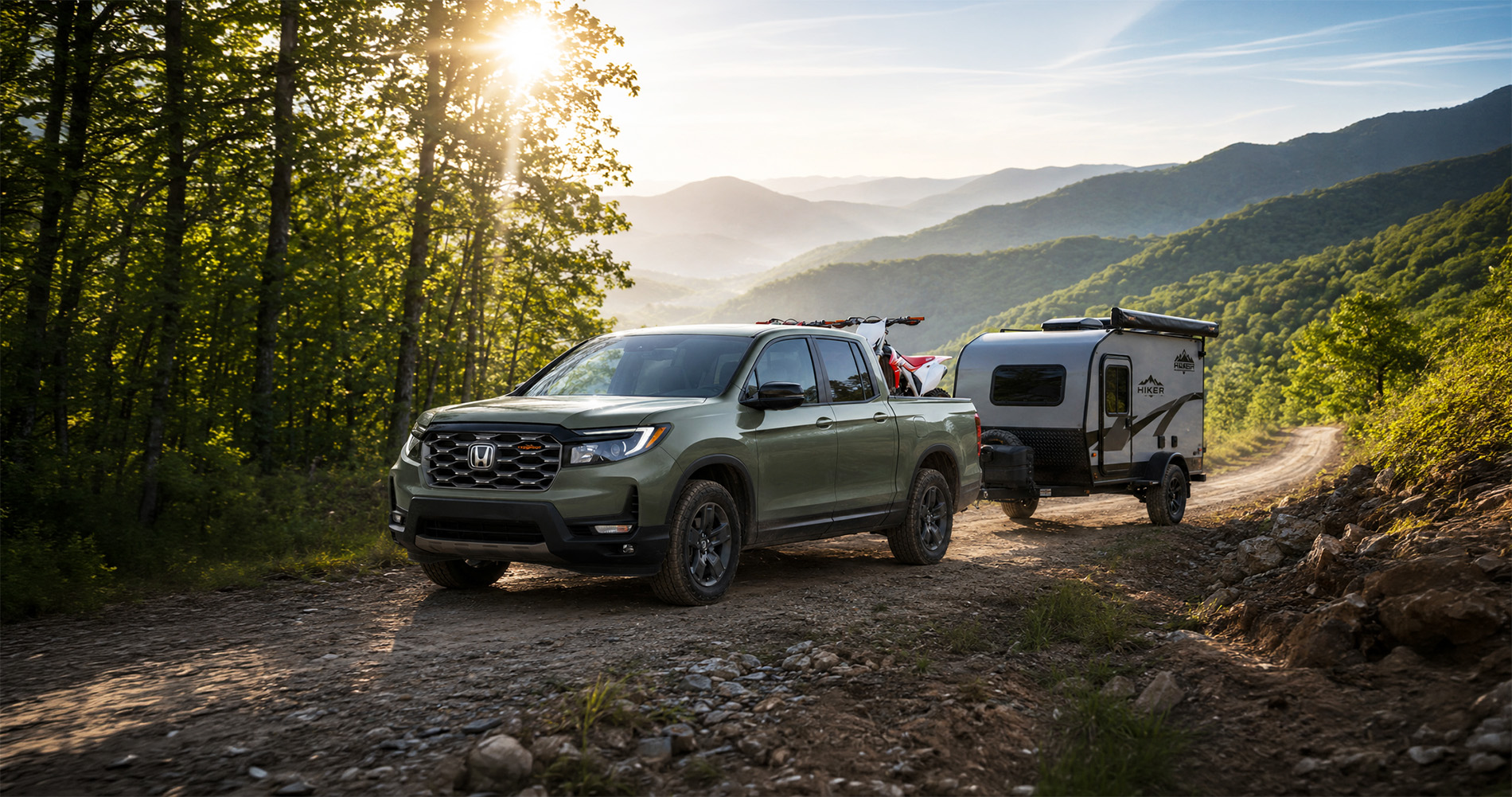 2026 Honda Ridgeline TrailSport trim towing an off road camper through the mountain with dirt bikes in the bed.