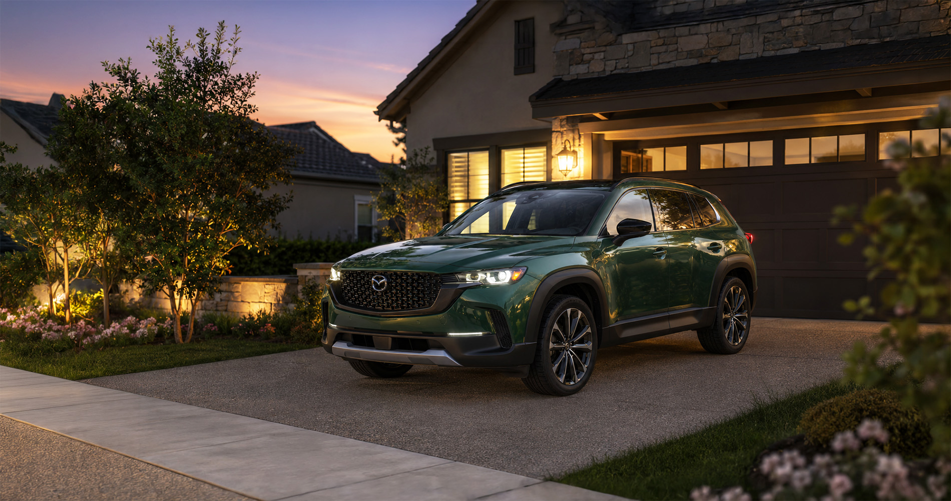 Green CX‑50 parked in a well‑lit suburban driveway at dusk, showcasing elegant styling and premium appeal.