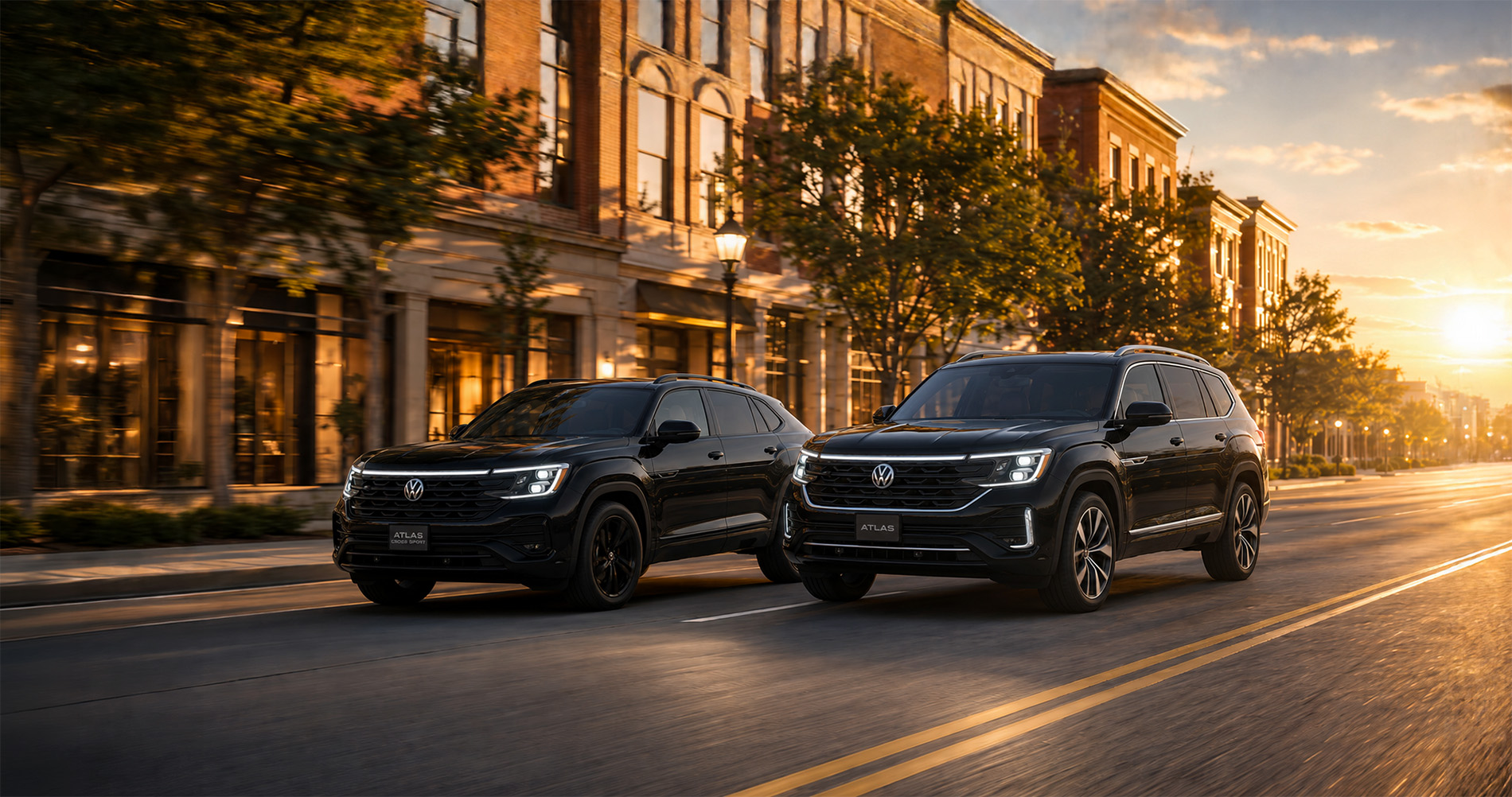 Two black Volkswagen SUVs—a 2026 Atlas and a 2026 Atlas Cross Sport—driving side by side through downtown Easton, Massachusetts, at dusk with streetlights and storefronts glowing warmly, showcasing their sleek styling and modern presence in an urban setting.