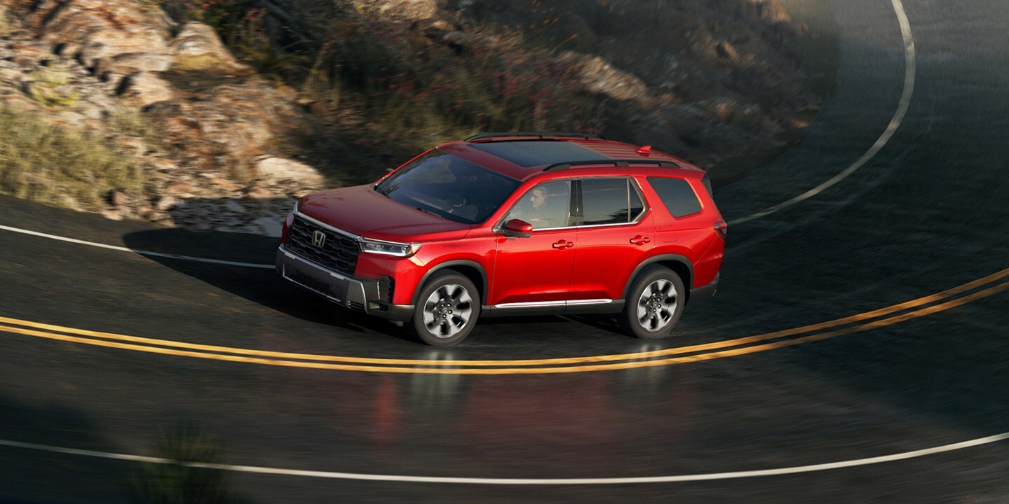 Red 2026 Honda Pilot driving through a curved mountain road, shown from above as a rugged three-row Honda SUV for RAV4 shoppers who need more space