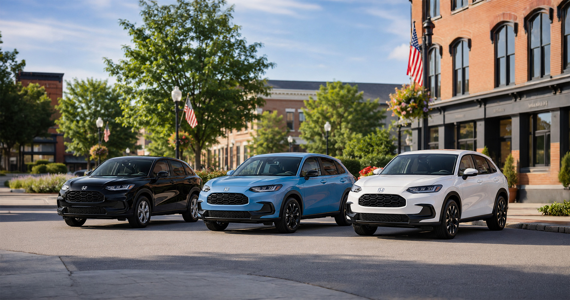 Three 2027 Honda HR-V SUVs in black, blue, and white parked side by side in a downtown area of Elizabethtown, Kentucky, with brick buildings, trees, and American flags in the background under bright morning sunlight.
