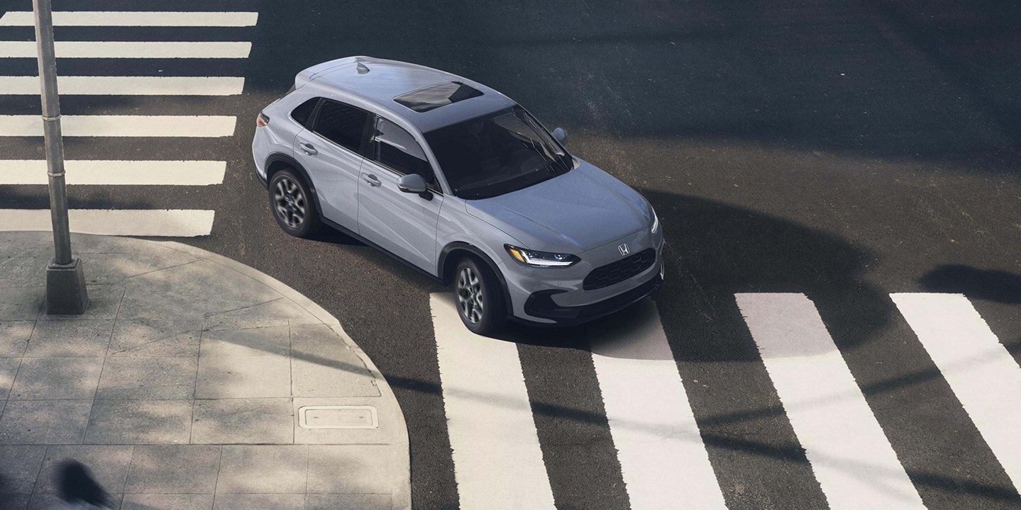 White 2027 Honda HR-V driving through a city crosswalk, shown from above as a compact Honda SUV for urban commuting and RAV4 shoppers who want something smaller