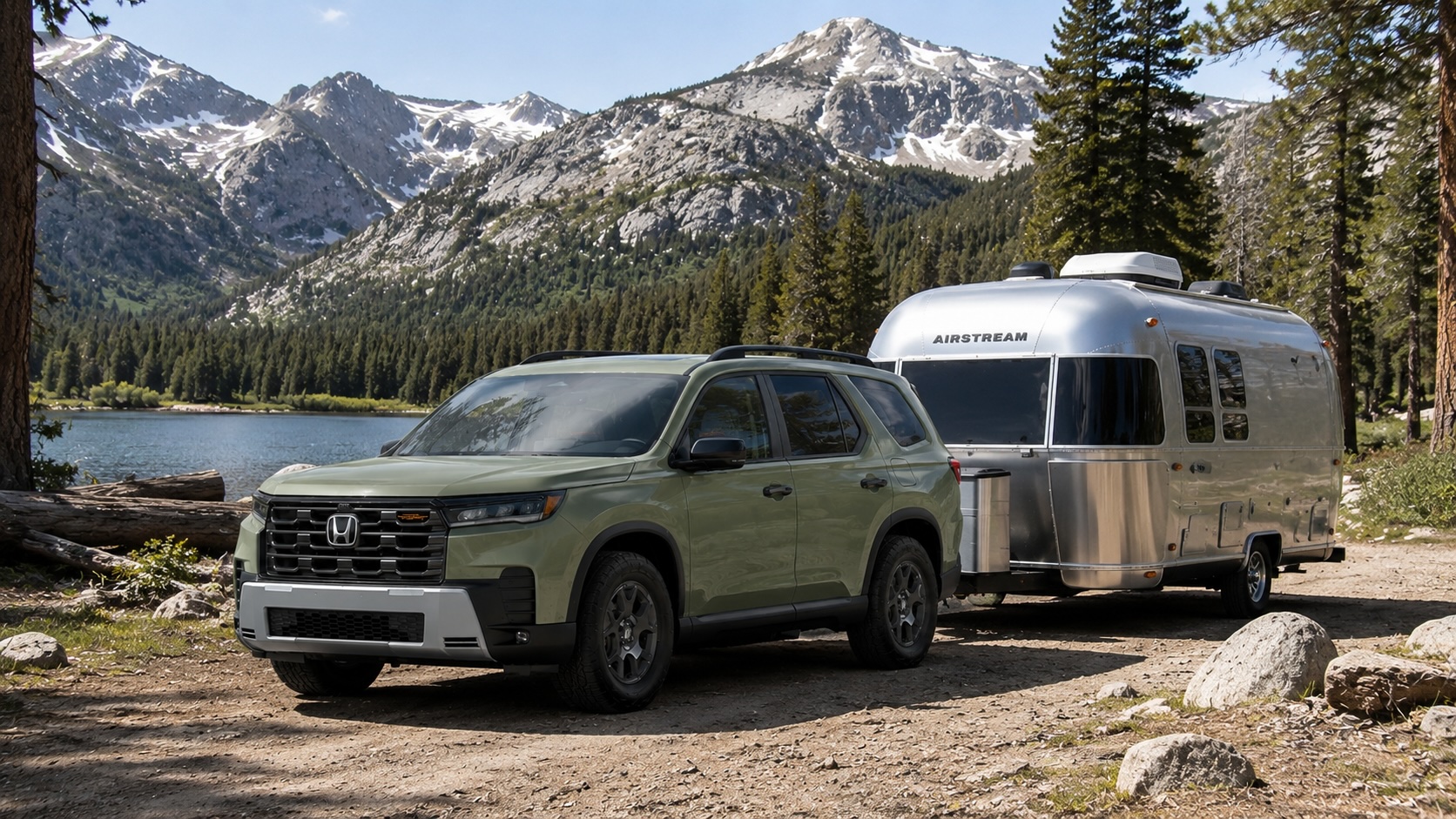 Olive green Honda Pilot towing a silver Airstream camper near a Sierra lake with pine trees and mountain peaks in the background.