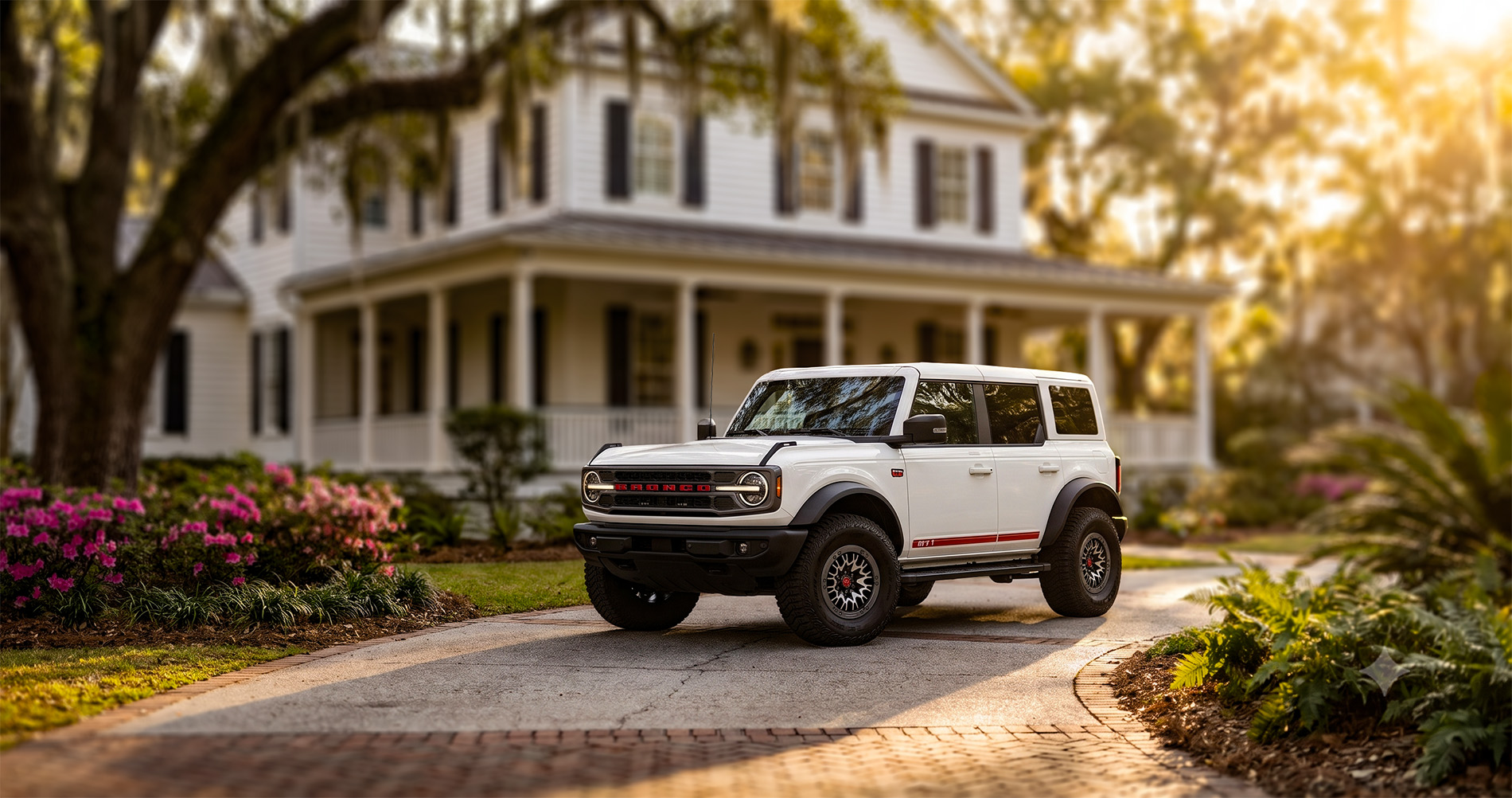 Wimbledon White Ford Bronco Outer Banks with the 60th Anniversary Package parked in a driveway at sunrise, highlighting red accents and heritage styling.