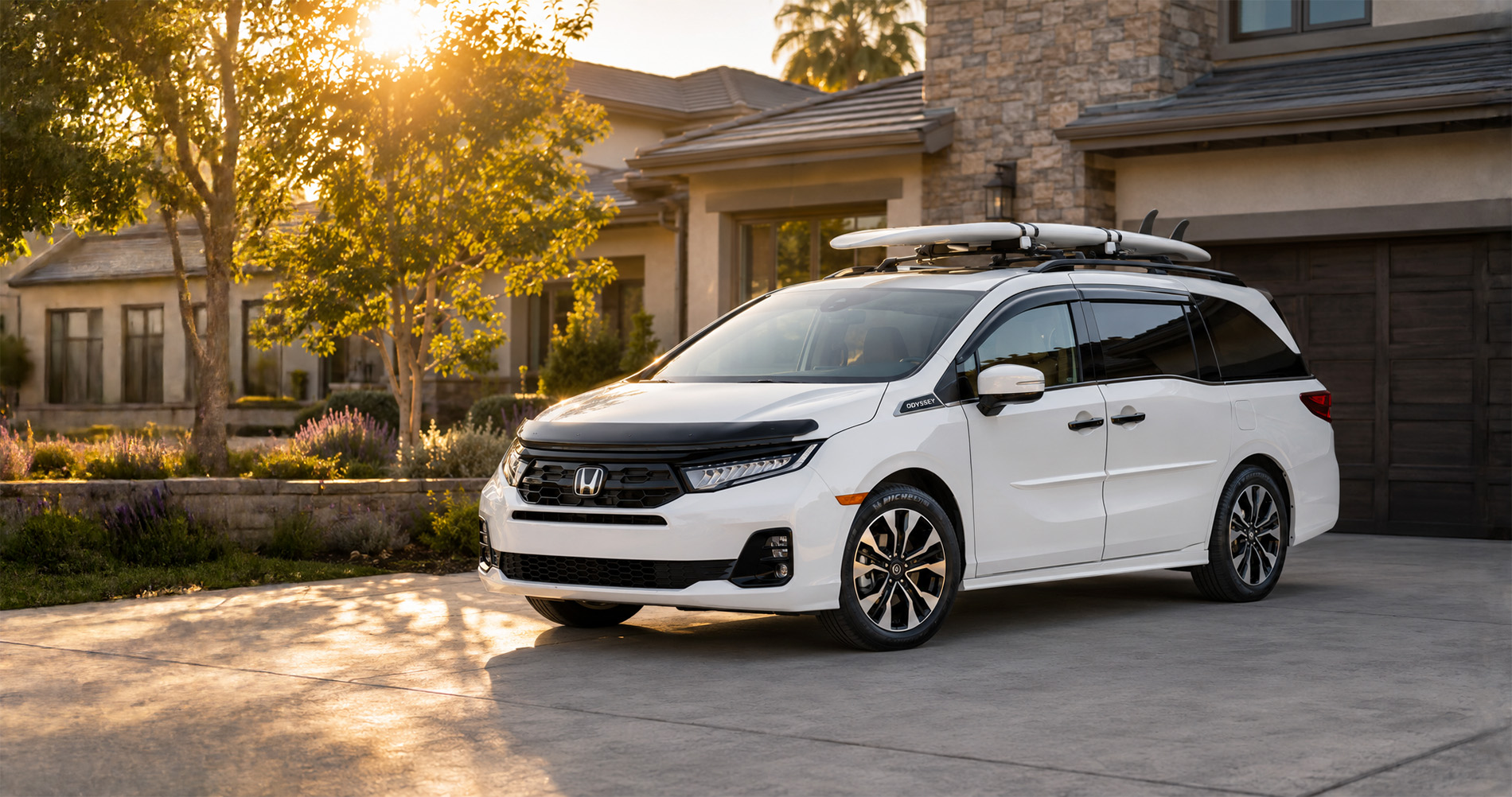White Odyssey parked in driveway at sunrise with surfboards on roof, highlighting family-friendly design.
