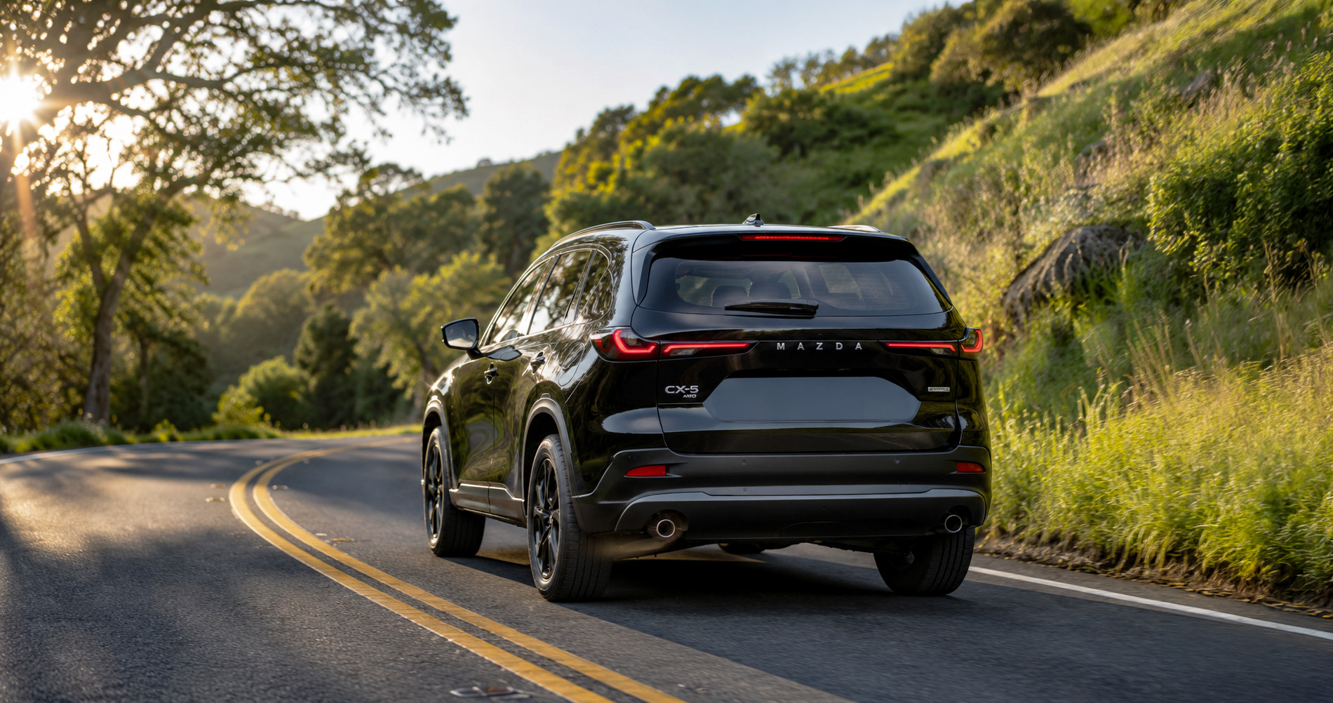 Black Mazda CX‑5 AWD driving on curved mountain road at sunset emphasizing taillight design and sporty stance.