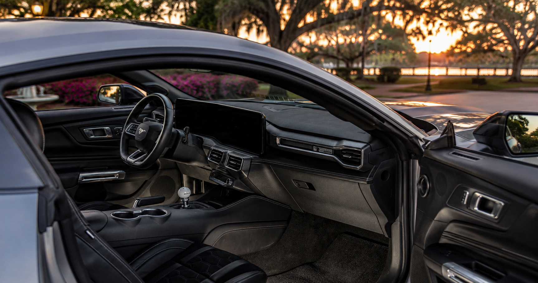 Black Shelby Mustang cabin with manual transmission digital display and leather seats overlooking waterfront at sunset highlighting driver focused design.