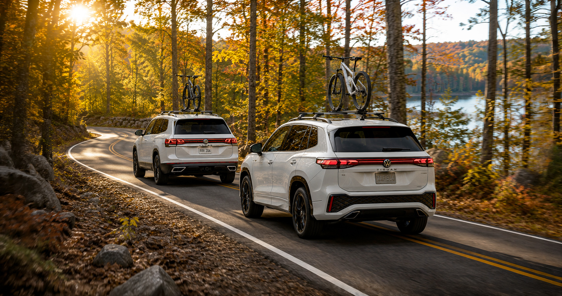 Volkswagen Atlas and Tiguan SUVs carrying bicycles while driving through a wooded Massachusetts setting.