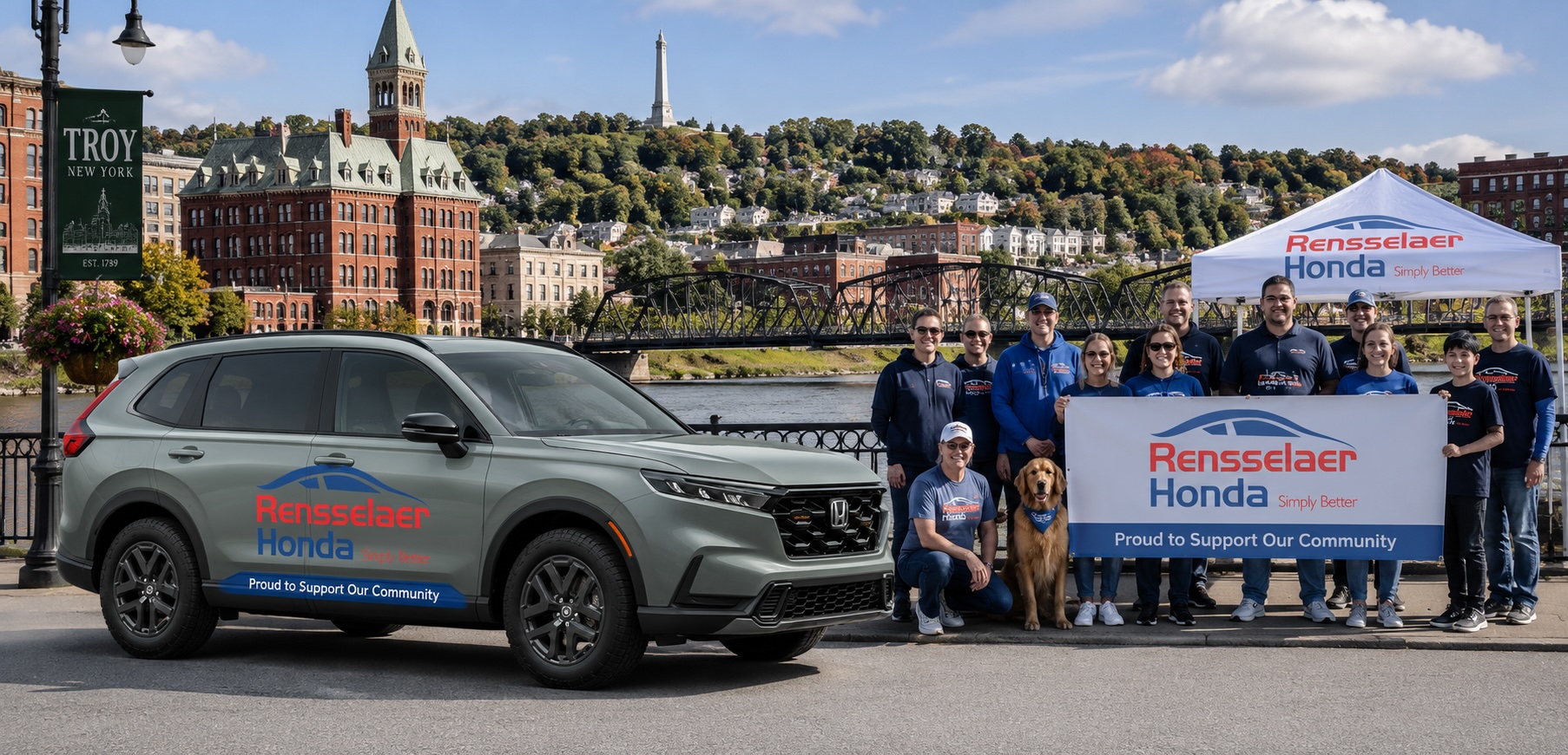 Rensselaer Honda team members gather with a Honda CR-V at a community event along the Troy, NY riverfront, with historic downtown Troy, the Hudson River, and recognizable local landmarks in the background.