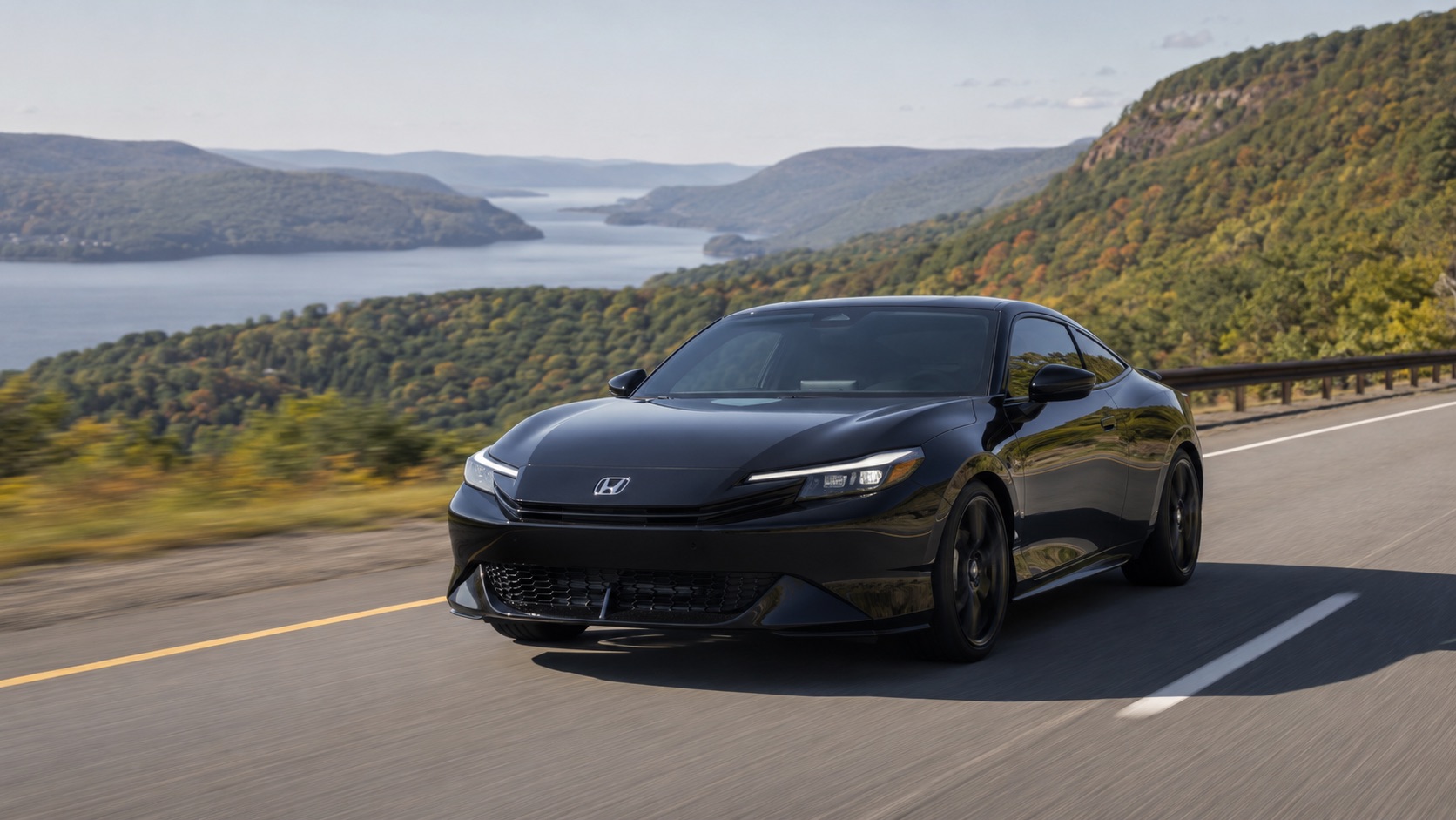 Black 2026 Honda Prelude Hybrid driving on a scenic Hudson Valley highway with river views and wooded hills in the background.