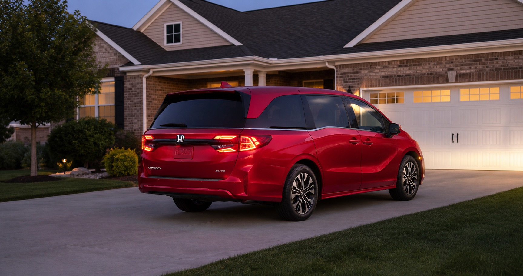 Red Honda Odyssey Elite parked in driveway at dusk in front of suburban home highlighting rear styling and LED taillights.