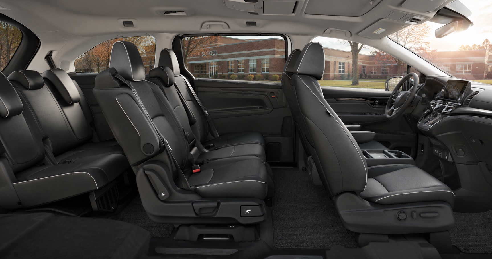 Black Honda Odyssey cabin showing three rows of leather seats and dashboard design with school building visible outside.