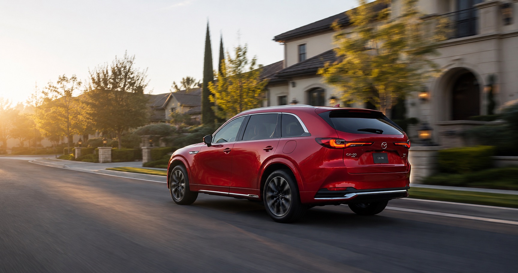 Red Mazda CX‑90 driving through upscale neighborhood at sunset emphasizing rear styling and premium presence.