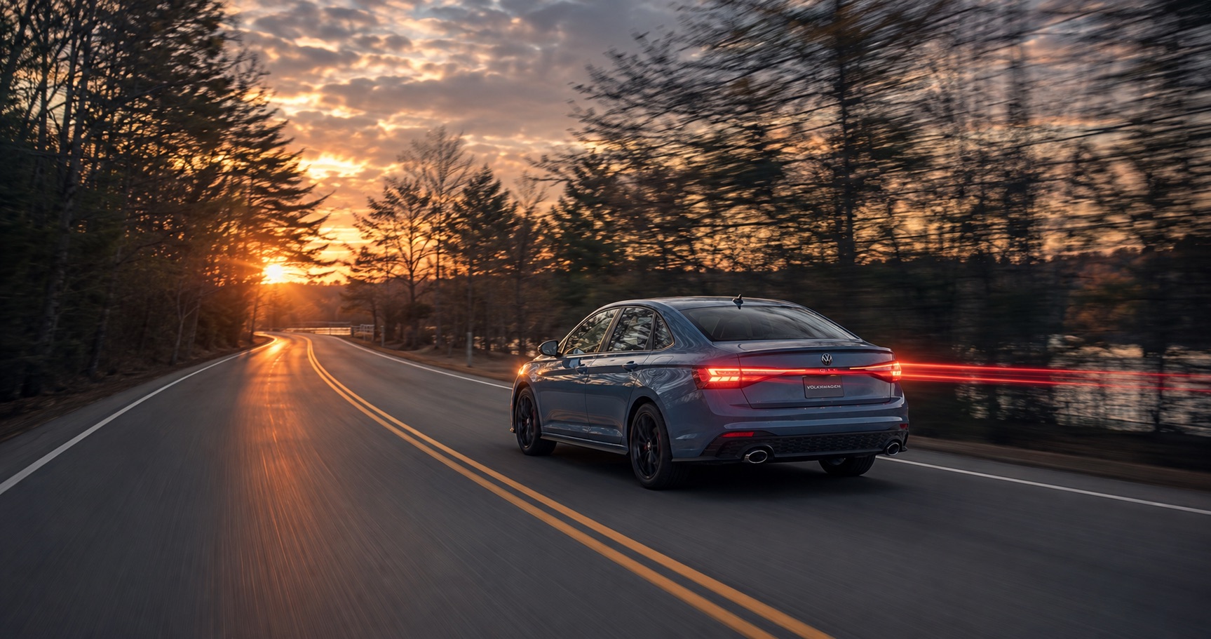 Blue Volkswagen Jetta GLI driving on a winding forest road at sunset, emphasizing rear styling, LED taillights, and performance character.