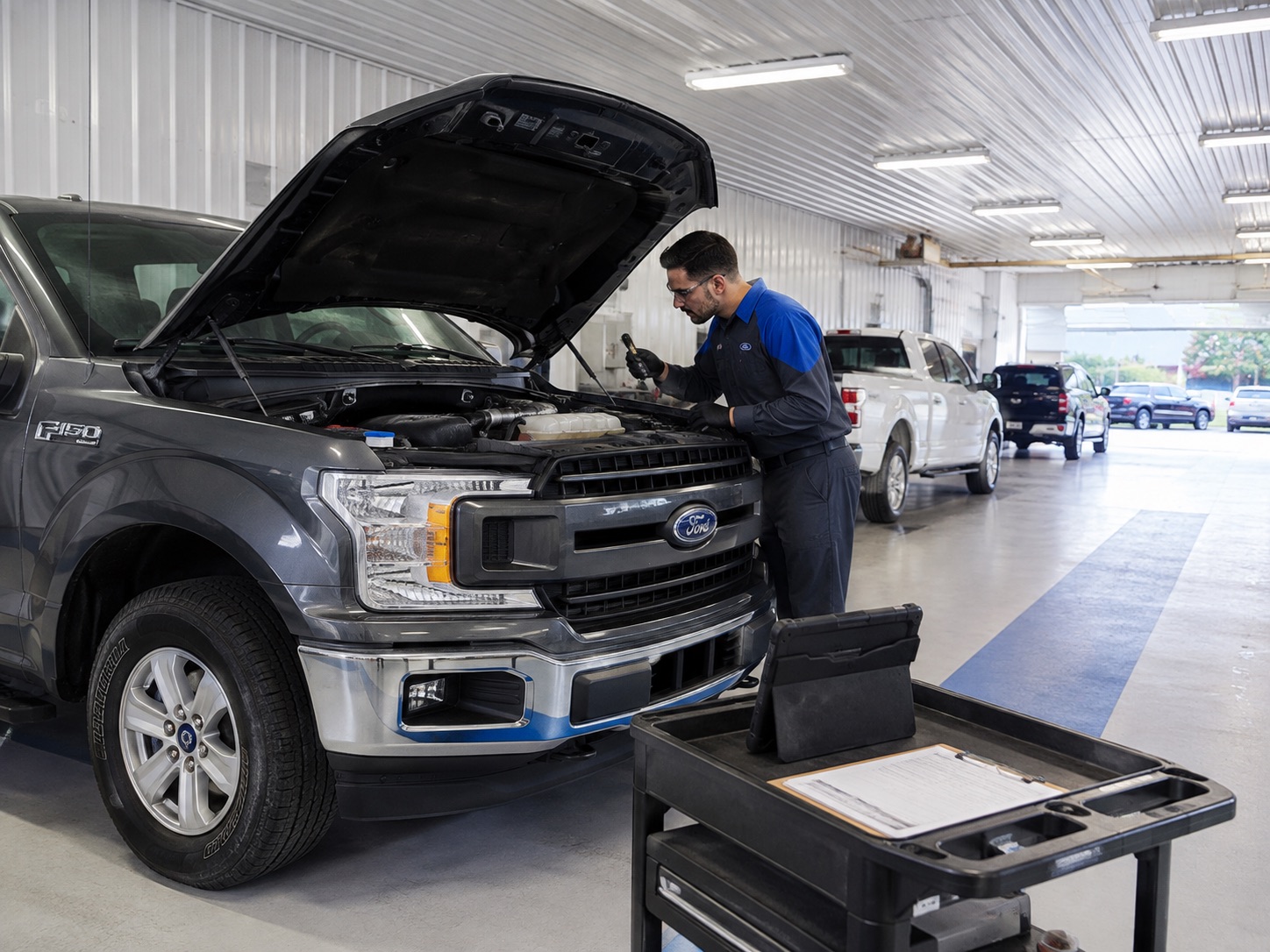 Ford technician inspecting the engine of a Ford F-150 during scheduled maintenance in a clean dealership service bay.
