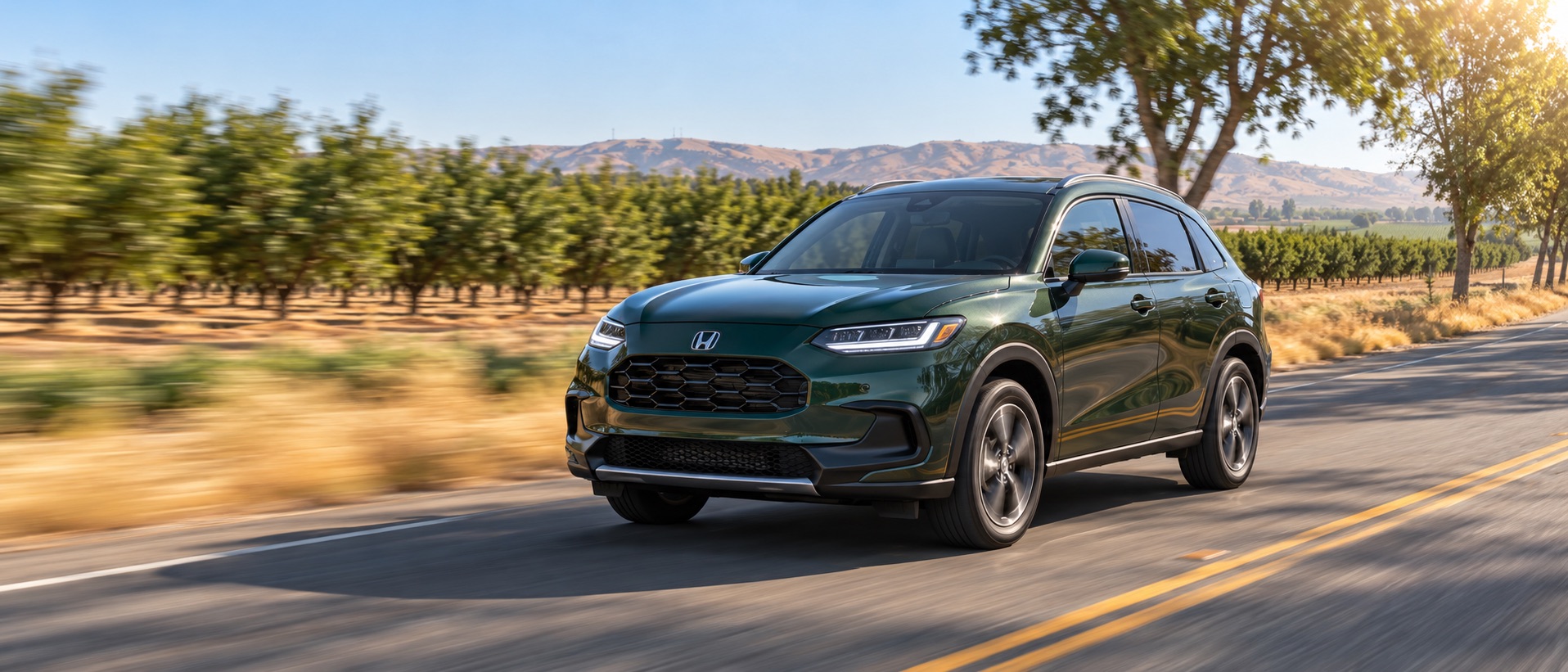 Nordic Forest Pearl 2027 Honda HR-V EX-L AWD driving along an orchard-lined road near Tracy, California, with agricultural fields and golden hills in the background